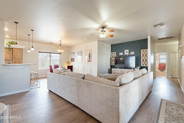 living room featuring a ceiling fan, wood finished floors, visible vents, and baseboards