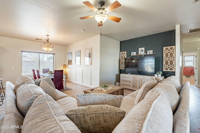 living area featuring a wealth of natural light, visible vents, a ceiling fan, and wood finished floors