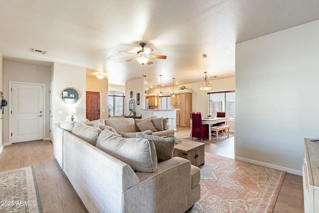 living area featuring light wood finished floors, visible vents, baseboards, a textured ceiling, and a ceiling fan