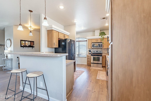 kitchen with a breakfast bar area, light wood finished floors, light countertops, appliances with stainless steel finishes, and backsplash