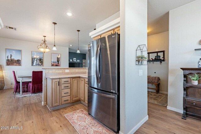 kitchen featuring light wood finished floors, a peninsula, light countertops, and freestanding refrigerator