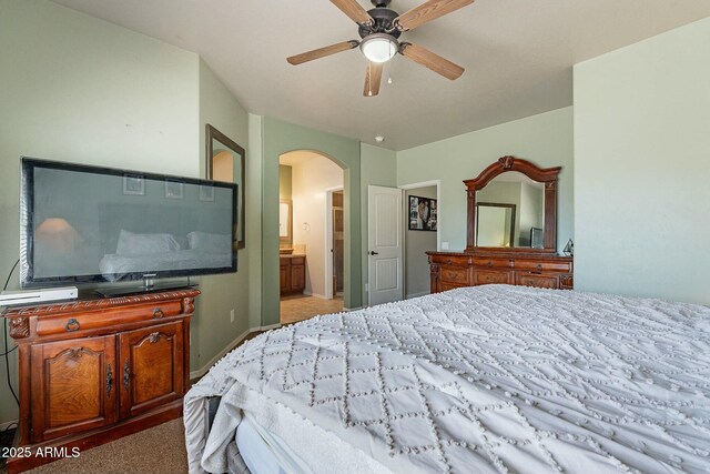 carpeted bedroom featuring connected bathroom, arched walkways, and ceiling fan