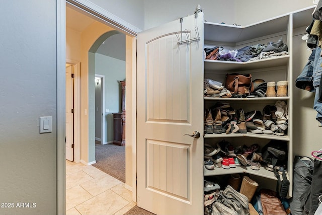 walk in closet with light tile patterned floors, arched walkways, and light colored carpet