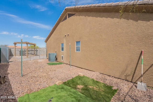 back of property featuring central AC unit, a tiled roof, fence, and stucco siding