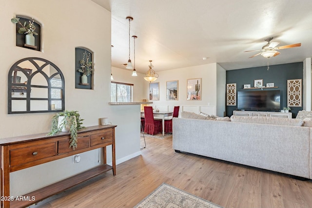 living area featuring baseboards, a ceiling fan, and light wood finished floors