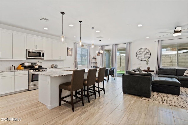 kitchen with appliances with stainless steel finishes, a kitchen bar, decorative light fixtures, a kitchen island with sink, and white cabinets