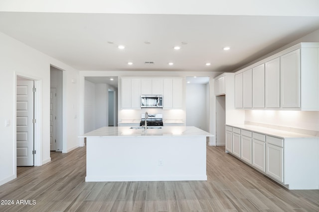 kitchen with an island with sink, sink, white cabinets, and light hardwood / wood-style flooring