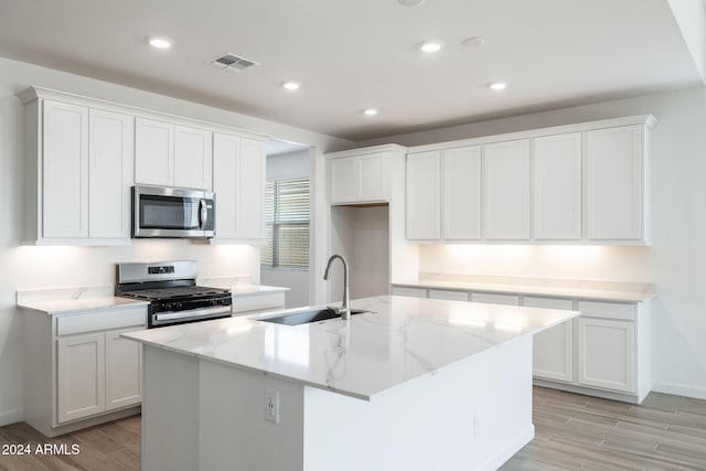 kitchen featuring sink, white cabinetry, a center island with sink, appliances with stainless steel finishes, and light stone countertops