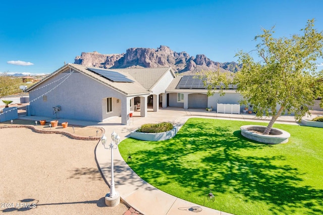 view of front of house featuring solar panels, a patio area, a mountain view, and a front yard