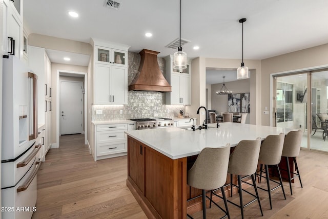 kitchen with stove, high end fridge, a sink, visible vents, and custom exhaust hood