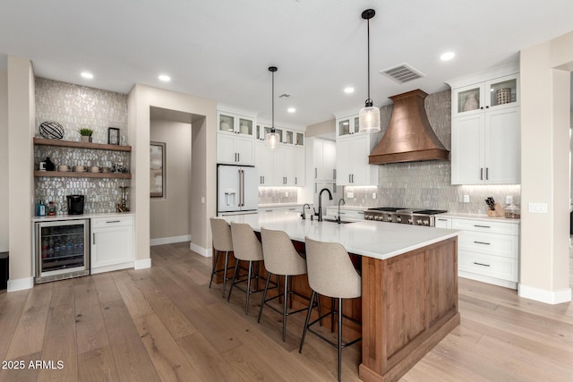 kitchen with wine cooler, custom exhaust hood, visible vents, light wood-style floors, and high end white fridge