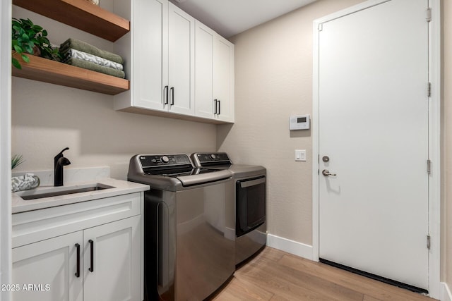 laundry area with washing machine and dryer, a sink, light wood finished floors, baseboards, and cabinet space