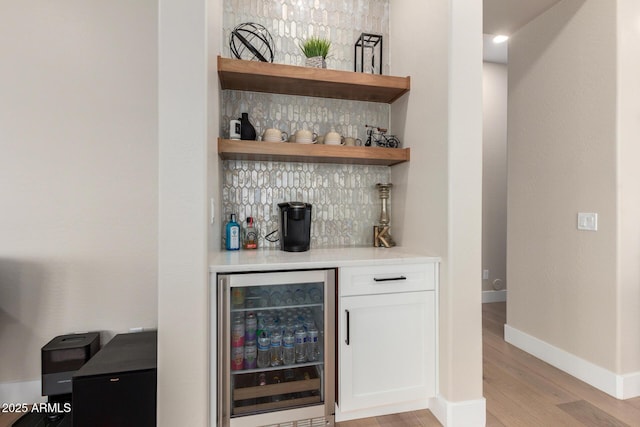 bar featuring a bar, baseboards, wine cooler, tasteful backsplash, and light wood-type flooring