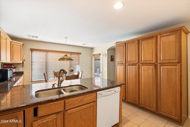 kitchen with dishwasher, sink, dark stone countertops, light tile patterned floors, and decorative light fixtures