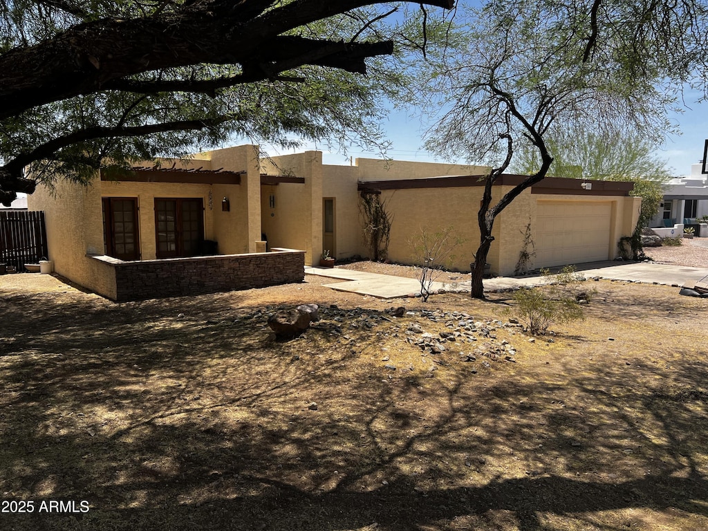 rear view of house with stucco siding, an attached garage, and driveway