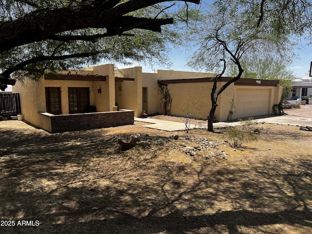 rear view of house with stucco siding, an attached garage, and driveway