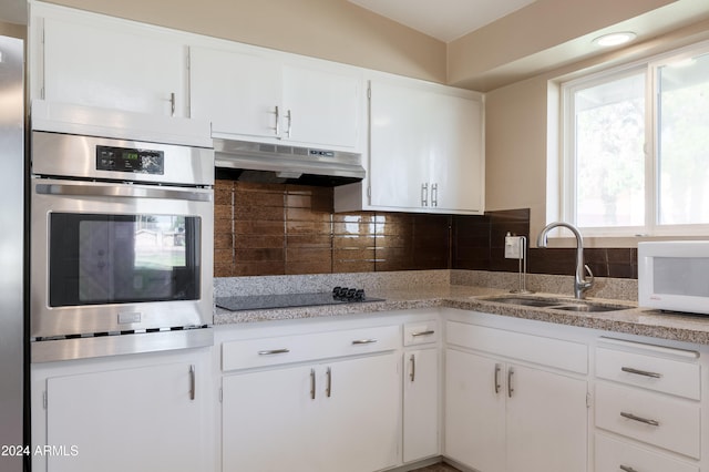 kitchen featuring stainless steel oven, sink, tasteful backsplash, black electric stovetop, and white cabinets