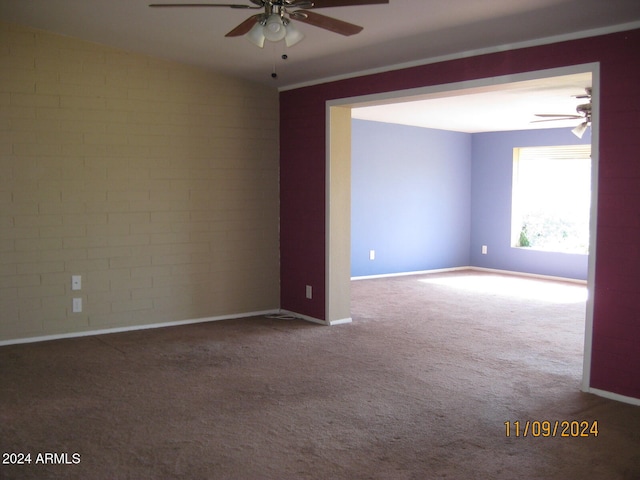 carpeted empty room featuring ceiling fan and brick wall