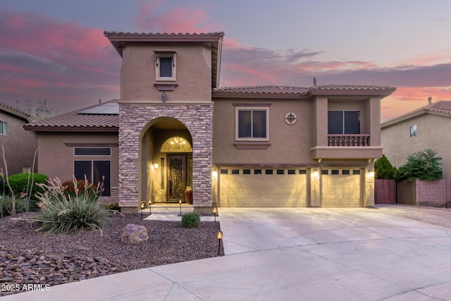 mediterranean / spanish-style house featuring stucco siding, a garage, stone siding, driveway, and a tiled roof