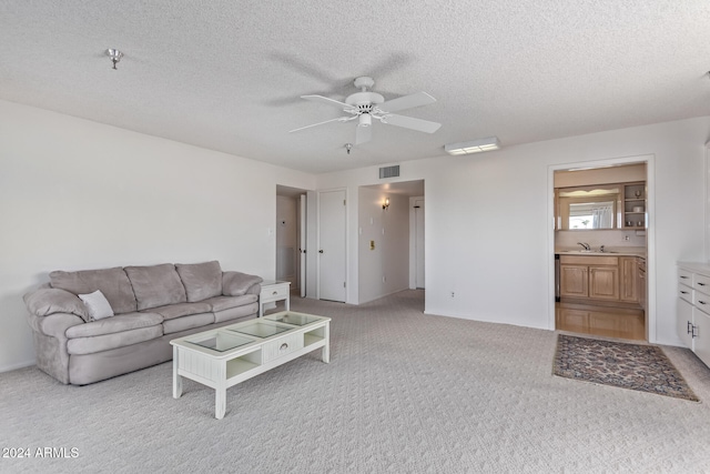 living room featuring a textured ceiling, light colored carpet, ceiling fan, and sink