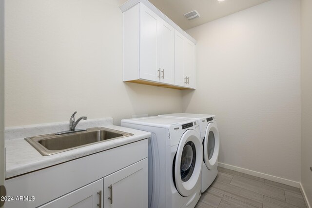 12568 W Orangewood Ave, Glendale, AZ 85307 - washroom featuring visible vents, cabinet space, a sink, baseboards, and separate washer and dryer