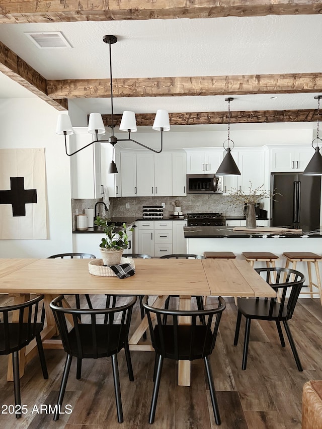 kitchen featuring dark hardwood / wood-style flooring, stainless steel appliances, beam ceiling, decorative light fixtures, and white cabinetry