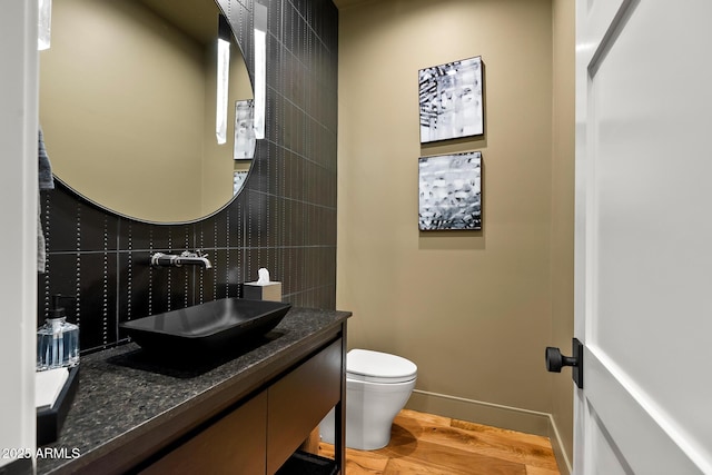 half bathroom featuring baseboards, toilet, decorative backsplash, wood finished floors, and vanity