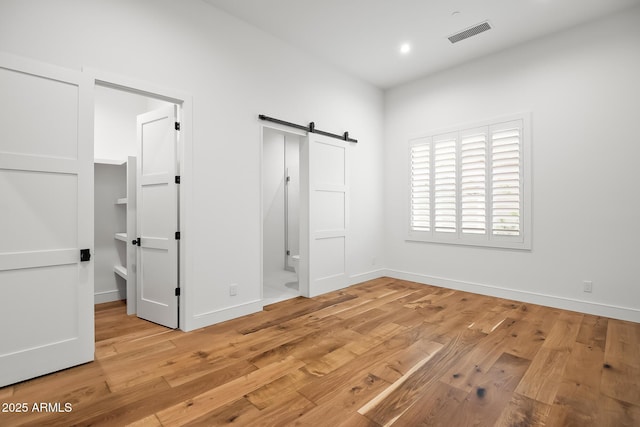 unfurnished bedroom with a barn door, baseboards, light wood-style floors, and visible vents