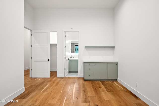 unfurnished bedroom featuring a sink, connected bathroom, baseboards, and light wood-style flooring