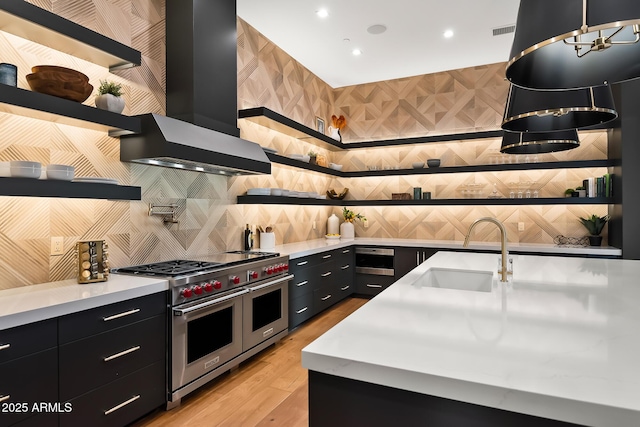 kitchen with wall chimney range hood, range with two ovens, dark cabinets, and a sink