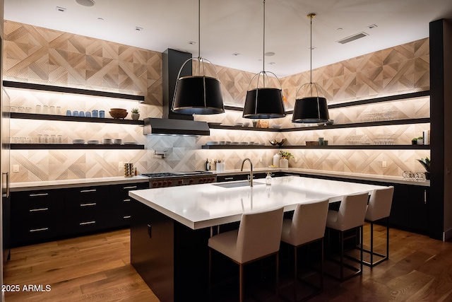 kitchen featuring dark cabinetry, a sink, light countertops, a kitchen bar, and wall chimney exhaust hood