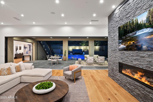 living area featuring wood finished floors, visible vents, recessed lighting, a stone fireplace, and stairs