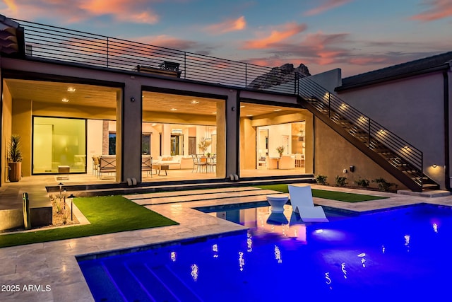 rear view of property featuring stucco siding, stairway, an outdoor pool, a balcony, and a patio area