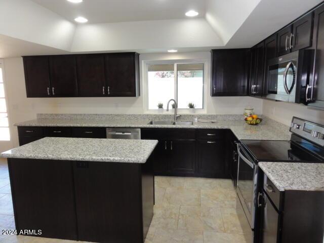 kitchen with a sink, a center island, appliances with stainless steel finishes, a raised ceiling, and dark cabinets