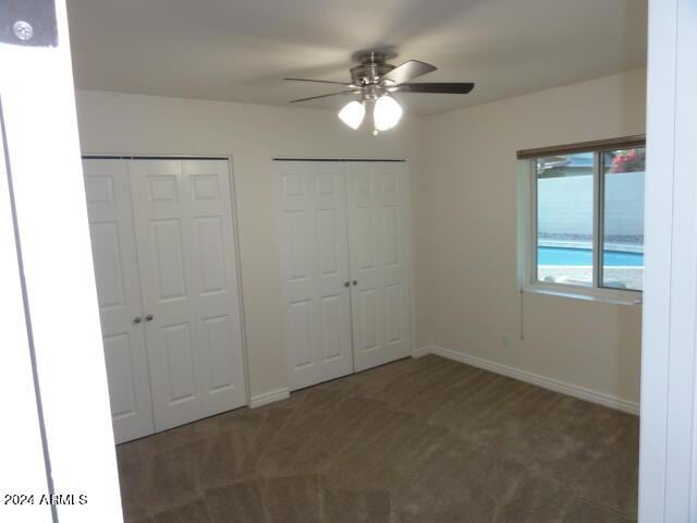 unfurnished bedroom featuring baseboards, two closets, ceiling fan, and carpet flooring