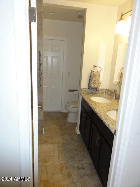 bathroom with double vanity, stone finish floor, toilet, and a sink