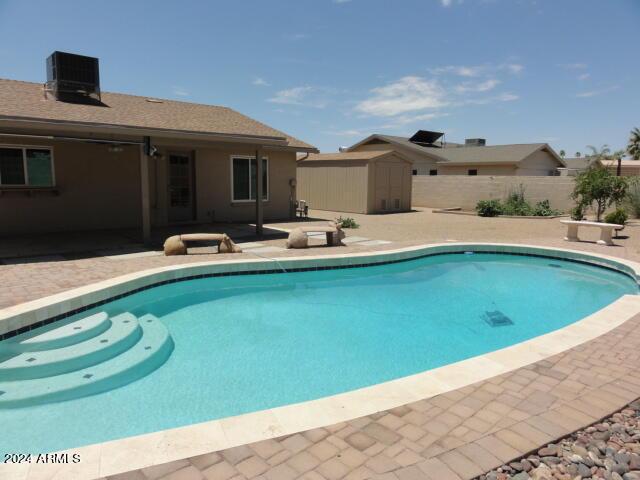 view of swimming pool with fence, a shed, central AC unit, an outdoor structure, and a patio area