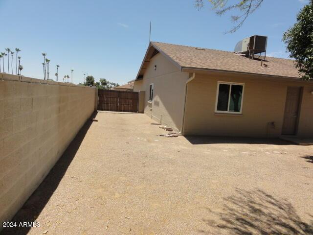 view of side of property with stucco siding, a gate, central AC, fence, and roof with shingles