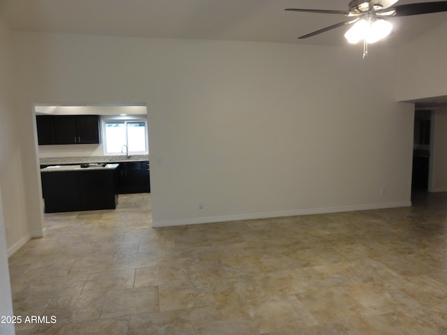 unfurnished living room with ceiling fan, baseboards, and a sink