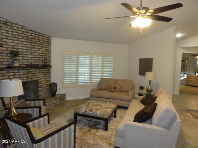 living room with baseboards, ceiling fan, a fireplace, and vaulted ceiling