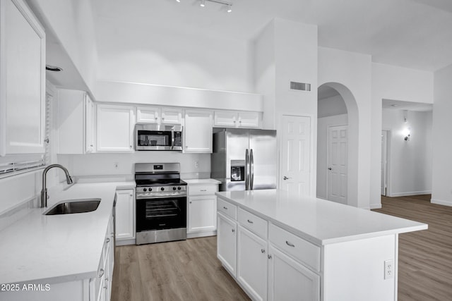 6368 W Firebird Dr, Glendale, AZ 85308 - kitchen featuring appliances with stainless steel finishes, a sink, arched walkways, white cabinetry, and light wood finished floors