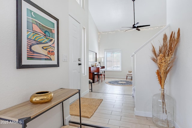 foyer featuring baseboards, ceiling fan, and a towering ceiling