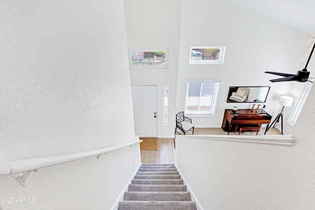 stairs with baseboards, a high ceiling, and a ceiling fan