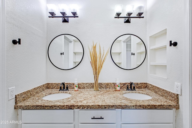 bathroom featuring a sink, built in shelves, a textured wall, and double vanity