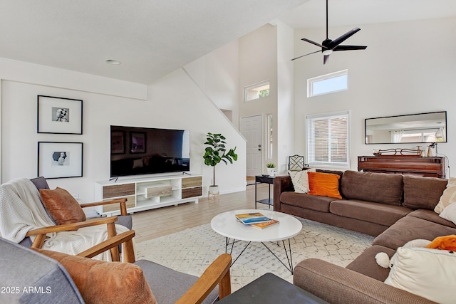 living area with ceiling fan, wood finished floors, baseboards, a high ceiling, and recessed lighting