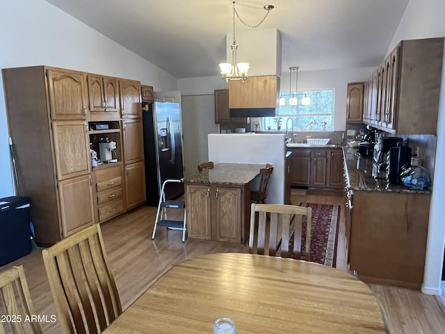 kitchen featuring lofted ceiling, dark stone countertops, stainless steel fridge, hanging light fixtures, and light hardwood / wood-style flooring