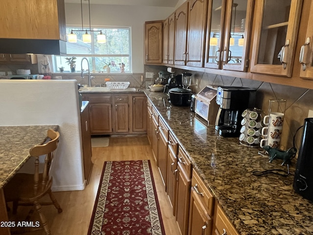 kitchen featuring pendant lighting, sink, dark stone countertops, backsplash, and light hardwood / wood-style floors