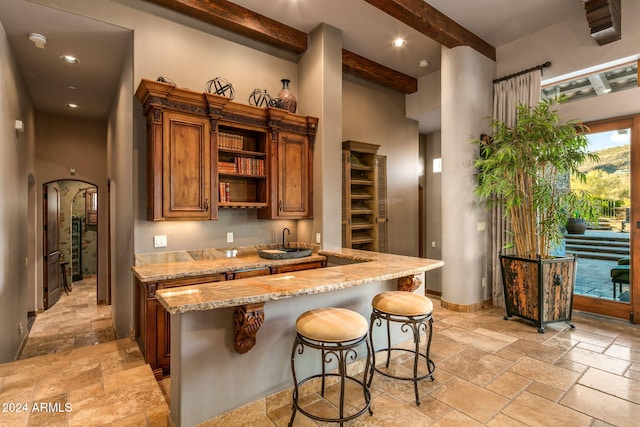 kitchen with a kitchen bar, light stone countertops, beamed ceiling, and a high ceiling