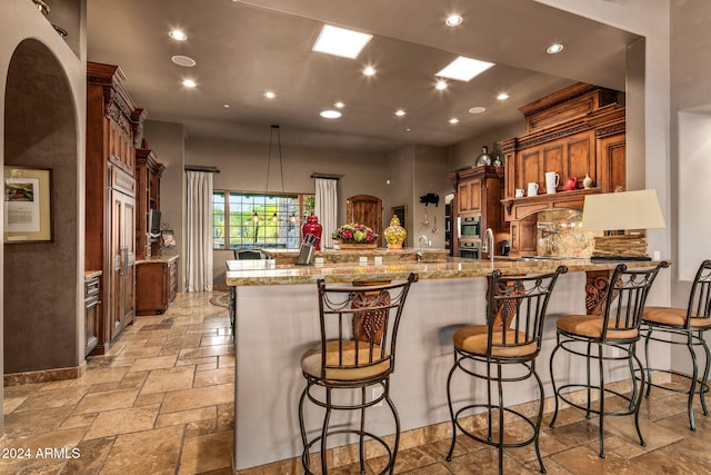 kitchen featuring sink, light stone counters, kitchen peninsula, decorative light fixtures, and a breakfast bar