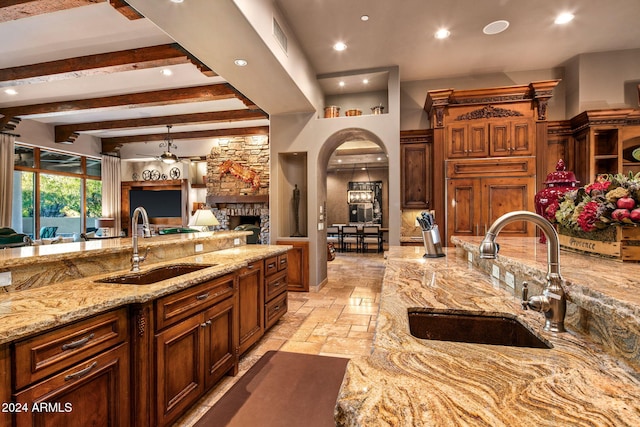 kitchen featuring beamed ceiling, light stone counters, a stone fireplace, and sink